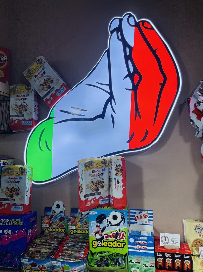 An illuminated wall sign shaped like Italy above a rack of Italian snacks, cropped away from the packaging lettering